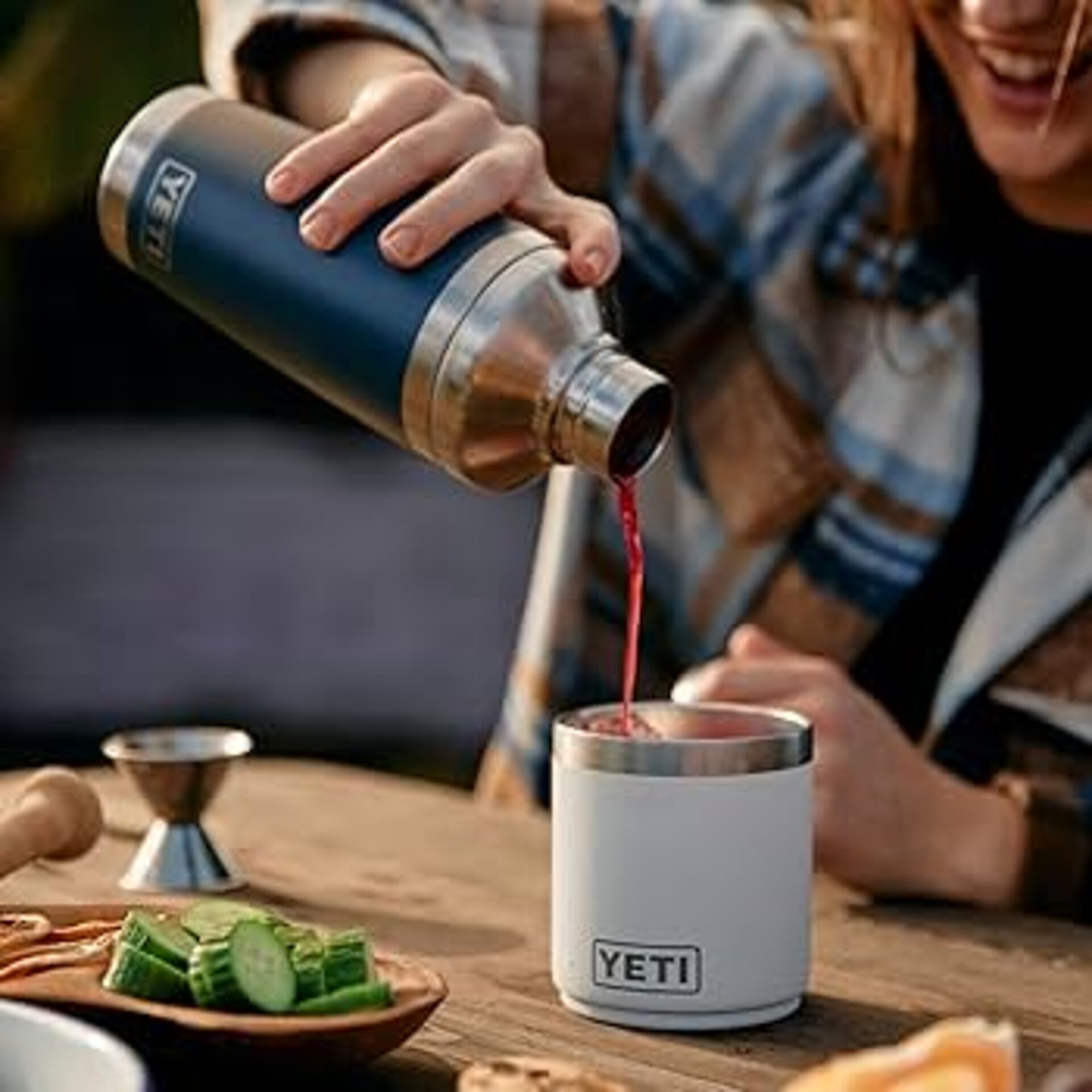 Frau gießt einen Coktail aus einem blauen Yeti Barkeeper Mixbecher Shaker in einen weißen Yeti wärmeisolierten Becher ein.