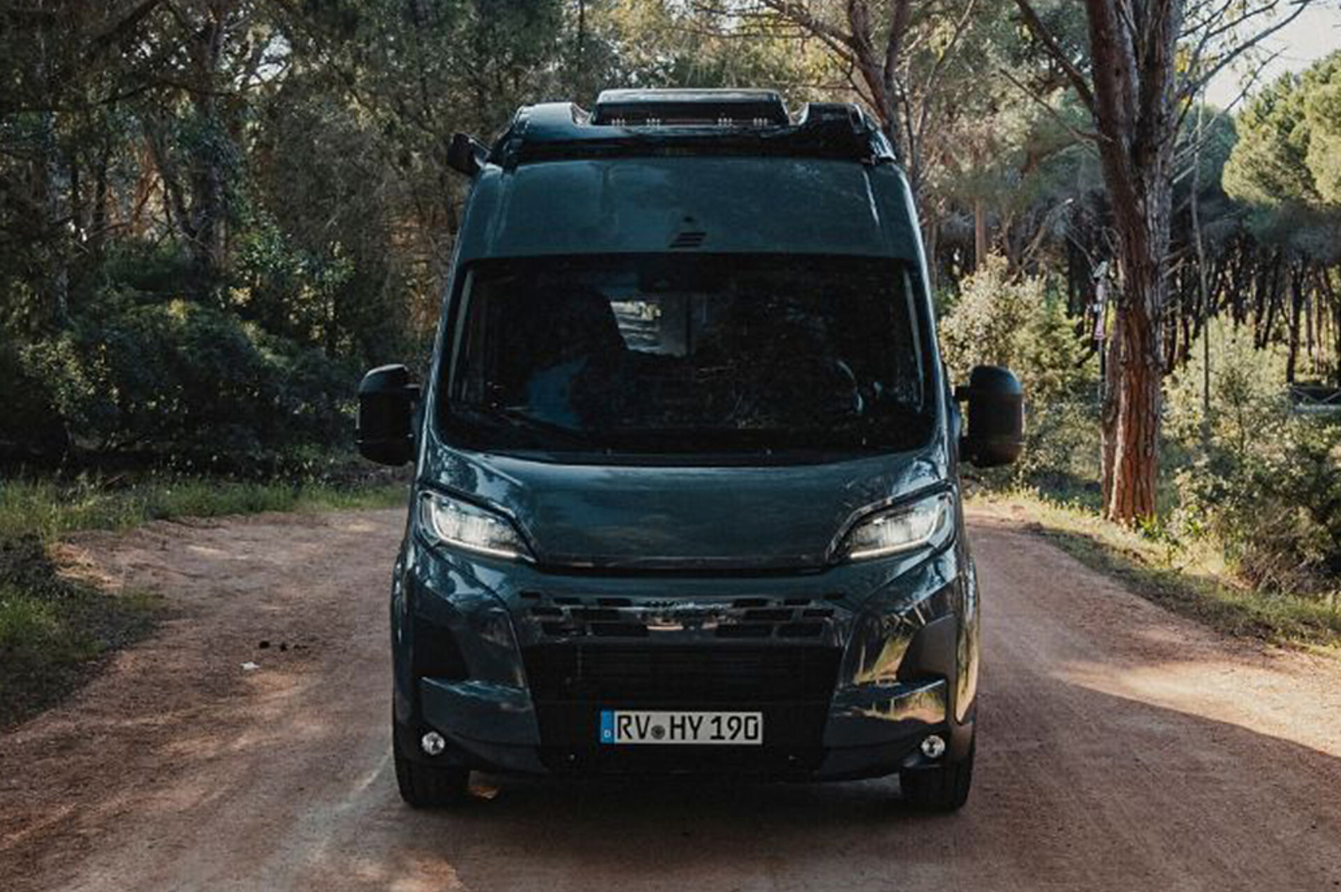 Dunkles Wohnmobil auf einer Straße in mediterraner Umgebung.