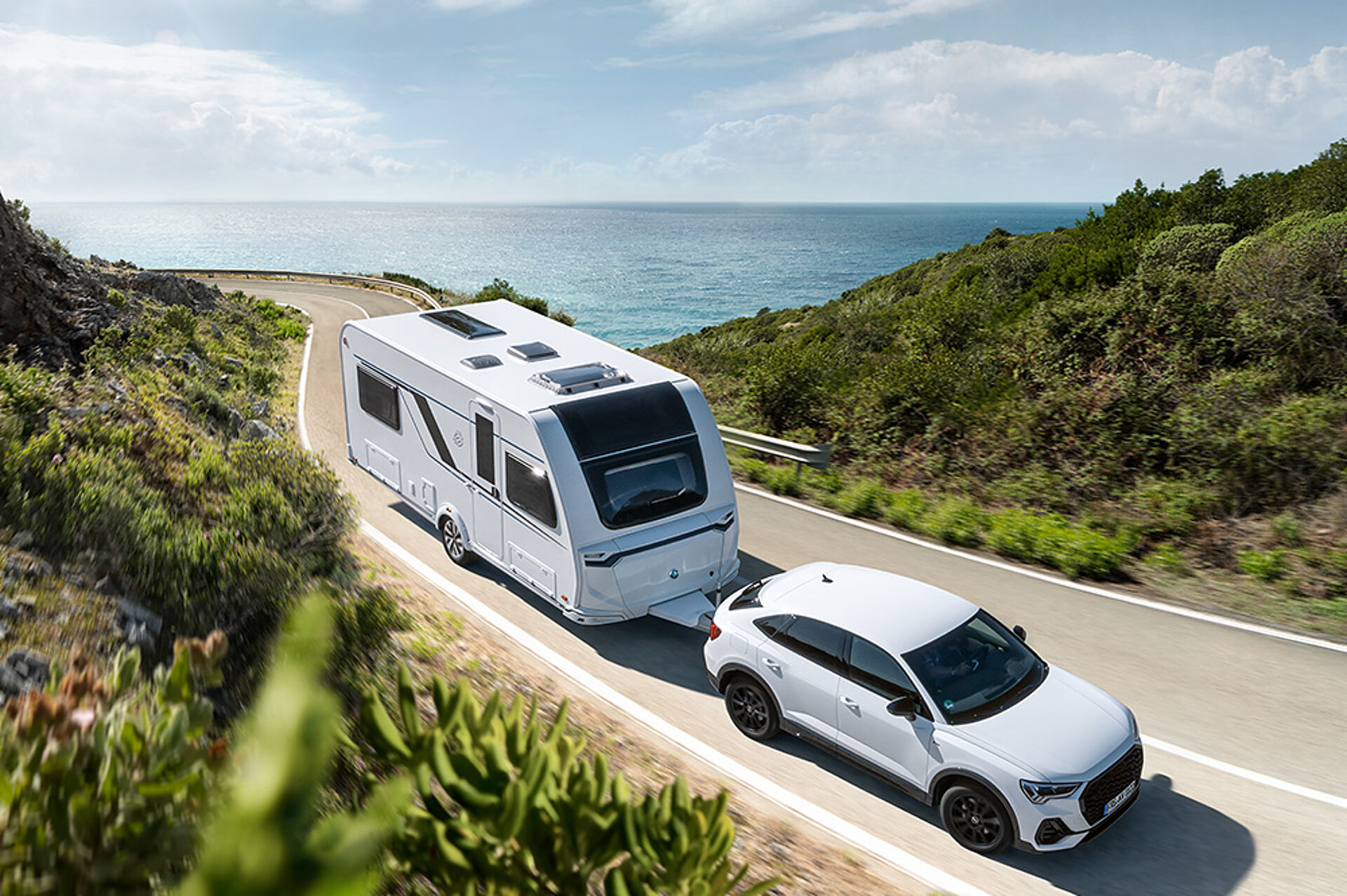 Een KNAUS-caravan rijdt langs een kustweg.