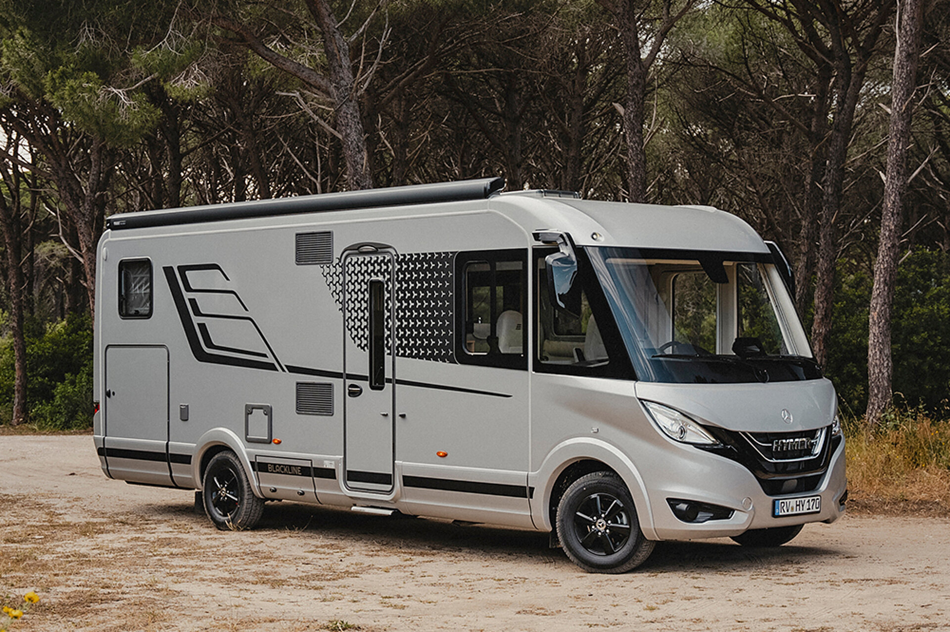 Ein HYMER B-ML I in BlackLine-Sonderedition parkt auf einem Platz vor einem Wald.