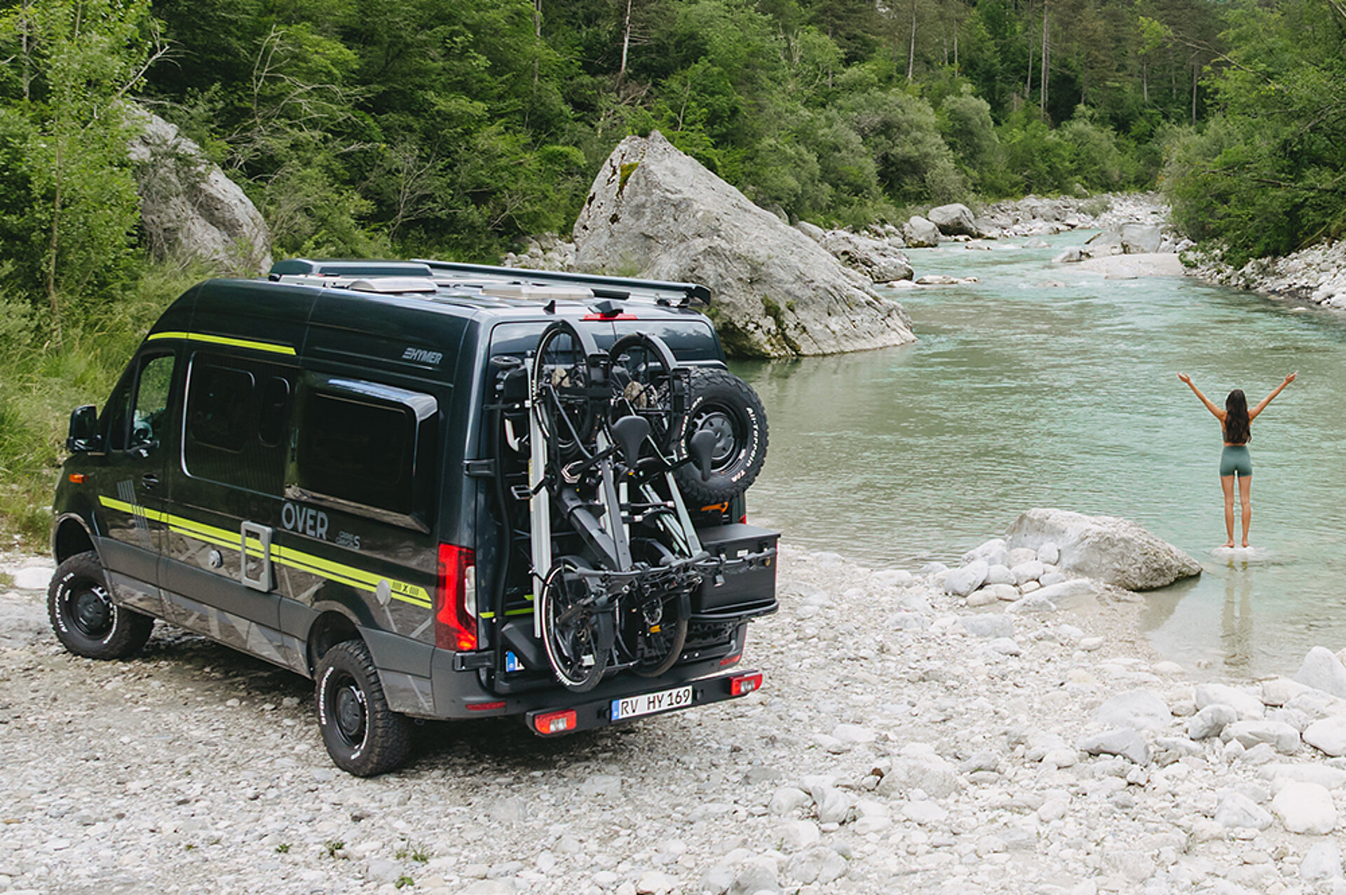 Ein HYMER Grand Canyon S CrossOver steht an einem Bergsee, eine Frau steht davor und breitet ihre Arme aus.