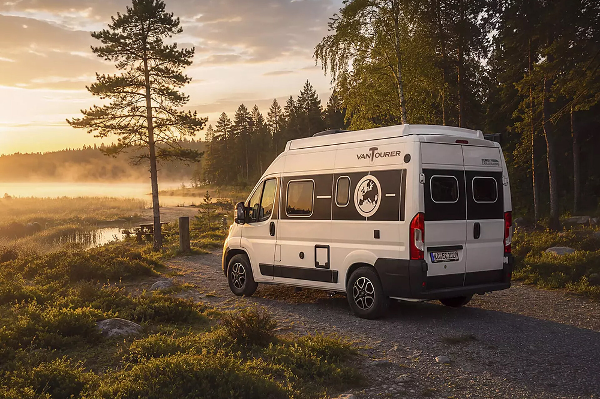 Ein weißer Camper Van vor einem See.