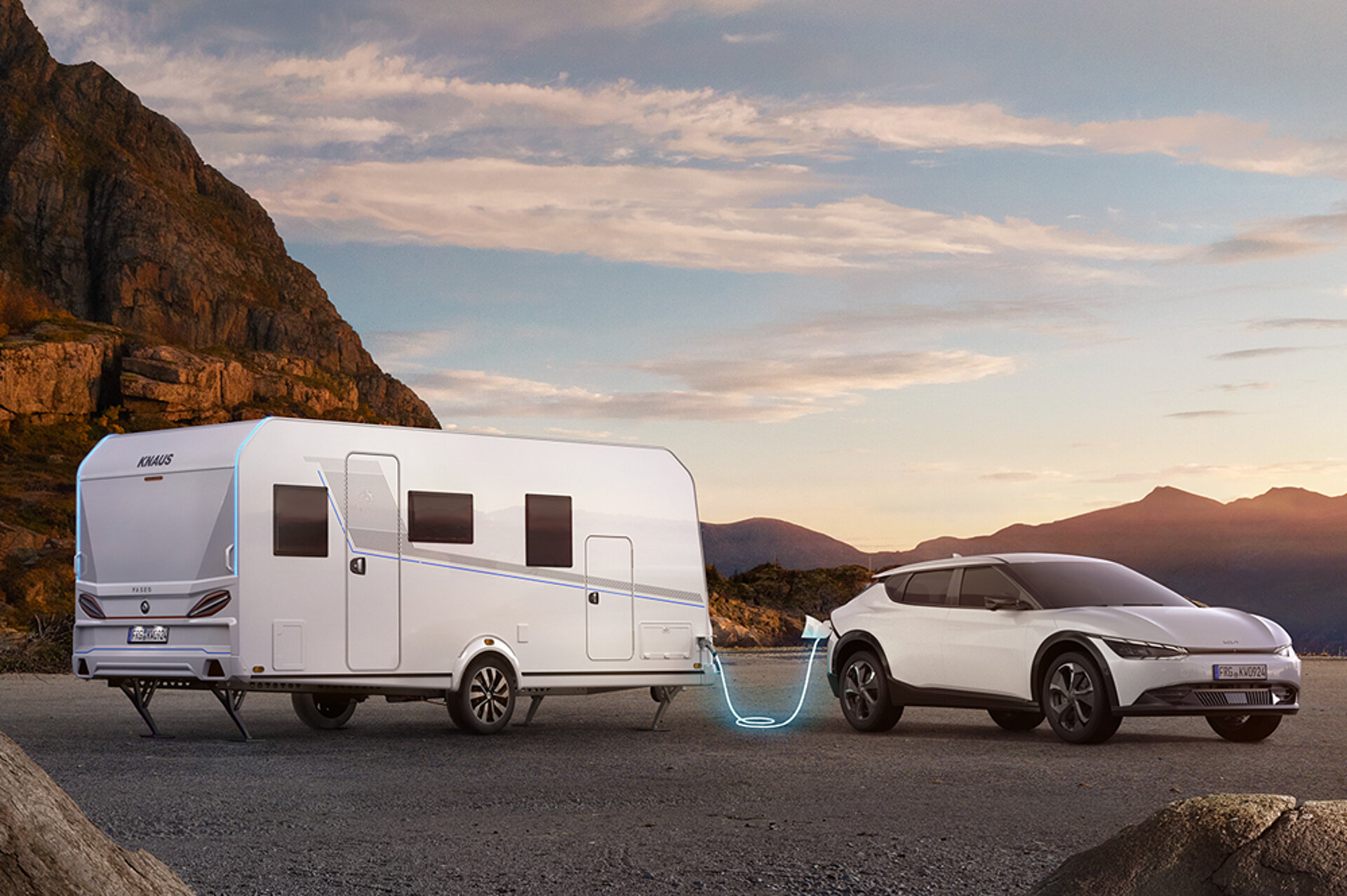 Une caravane blanche est stationnée avec une voiture blanche devant une montagne.