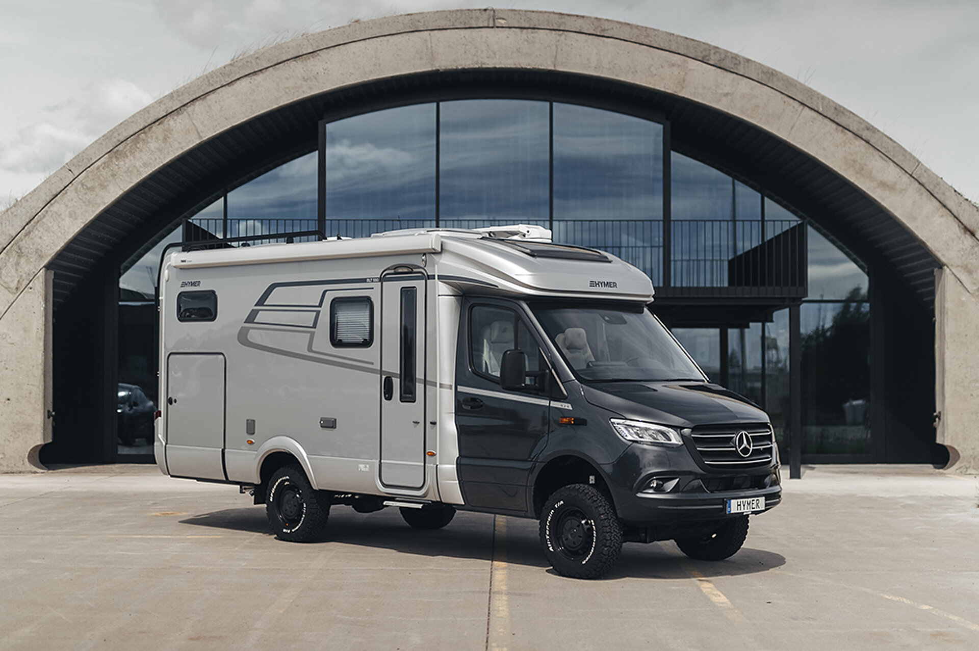Ein HYMER ML-T 580 steht vor der Glasfront eines runden Gebäudes.