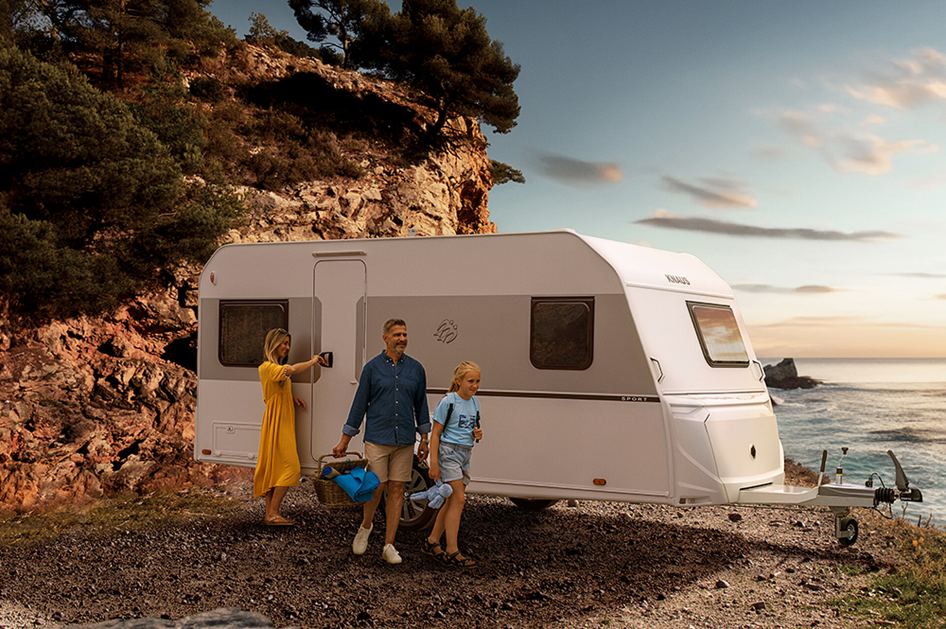 Een witte caravan op een strand met mensen op de voorgrond.