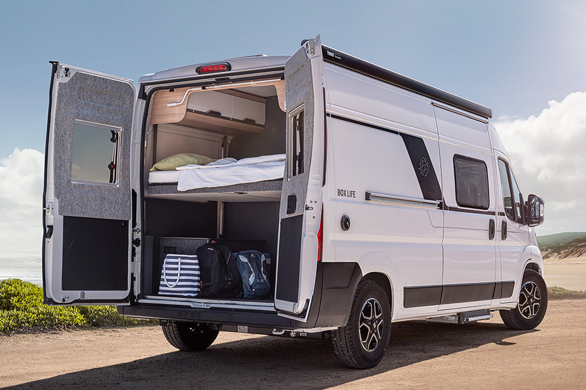 A white camper van stands in the desert with its rear door open.