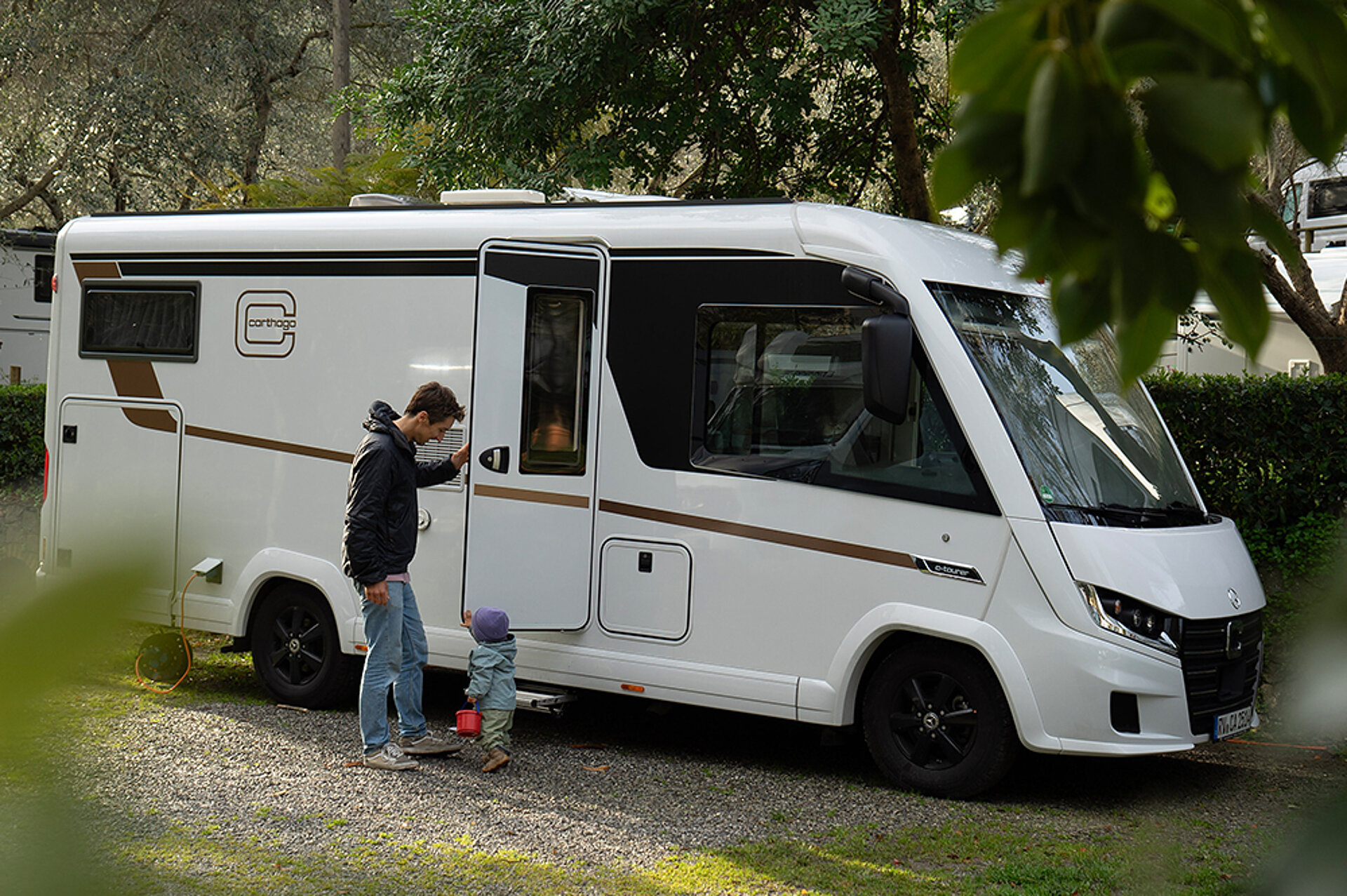 Mann und Kind stehen an einem weißen Wohnmobil und öffnen eine Tür.