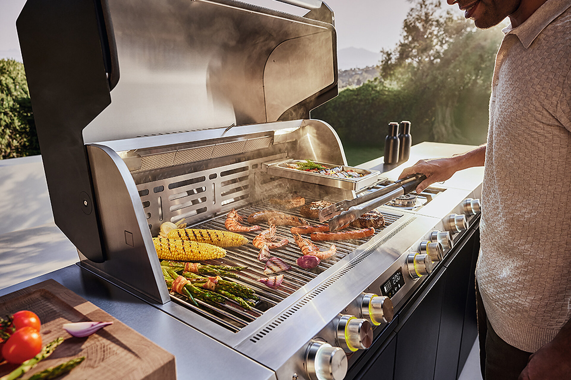 Bild von einer geöffneten Outdoorküche mit Grillgut auf dem Rost.