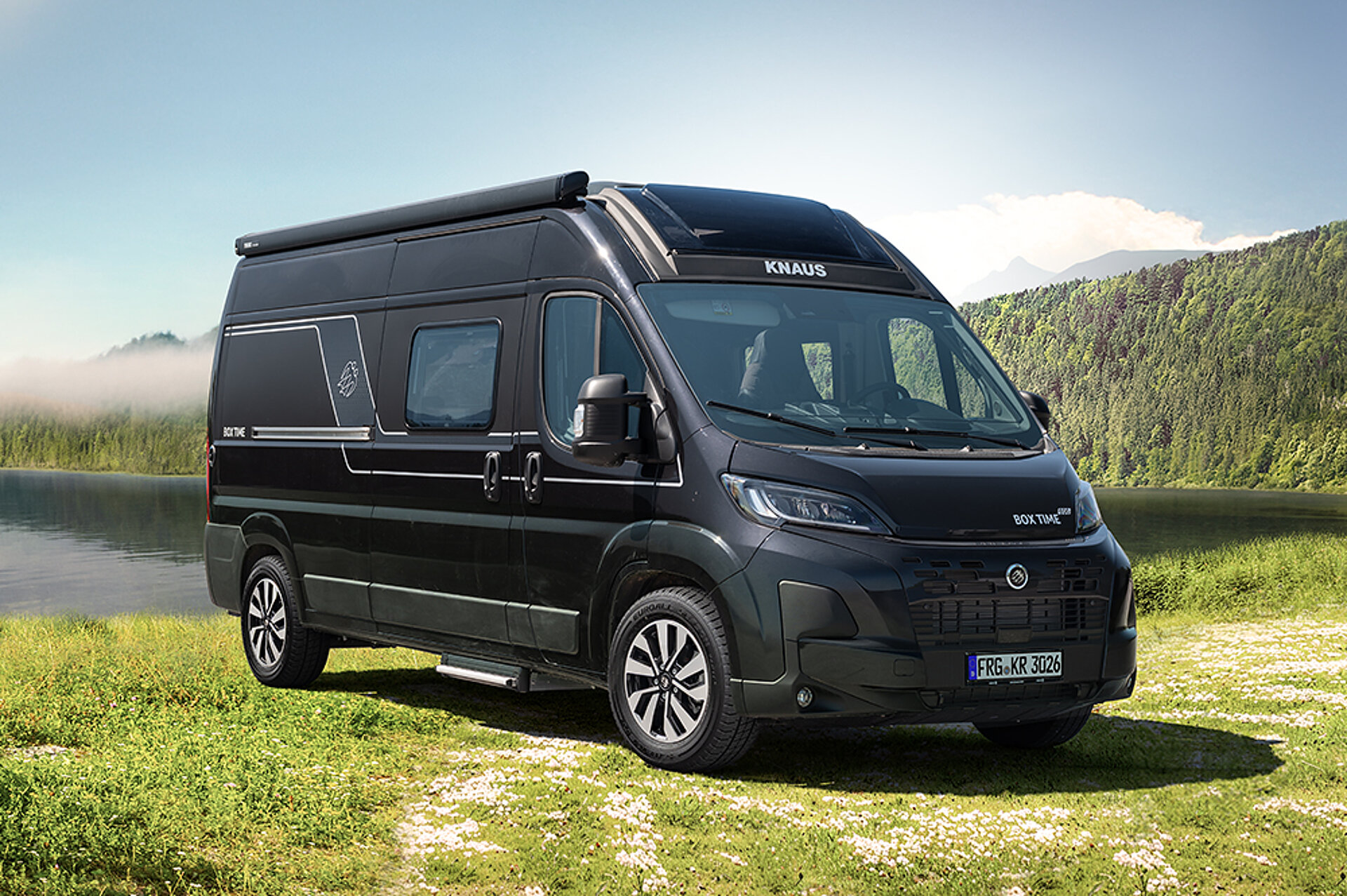 A dark camper van stands in a mountain landscape on a meadow.
