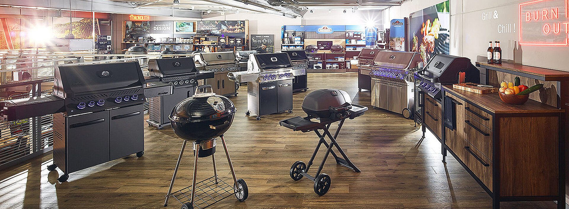 Gesamtansicht der Ausstellungsfläche von Napoleon. verschiedene Grillmodelle z.B Prestige, Rogue, Freestyle und TravelQ schön aufgereiht. Im Vordergrund auf der rechten Seite steht eine Outdoor Küche von Burn Outdoor Küchen mit Napoleon Prestige Gasgrill