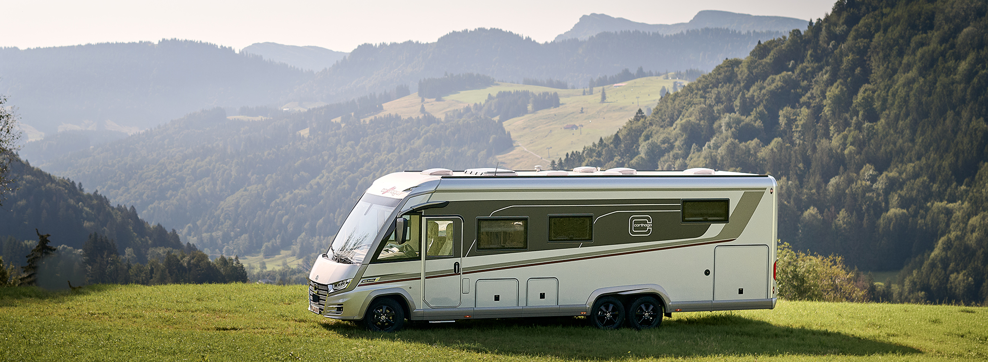 Weißes Reisemobil auf einer Wiese in den Bergen.