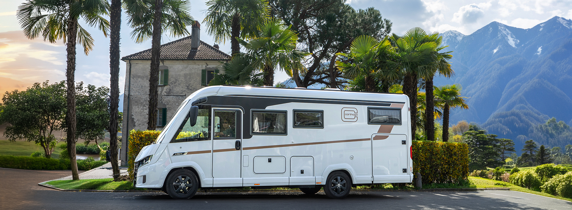 Weißes Carthago-Wohnmobil vor einem Haus mit Bäumen.