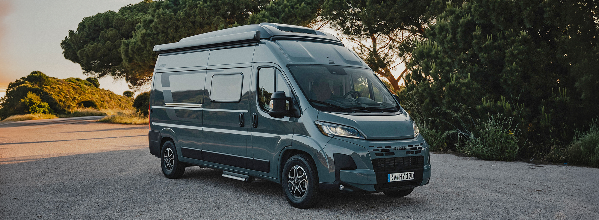Ein HYMER Redwood Camper Van steht auf einem Parkplatz vor einem Wald.