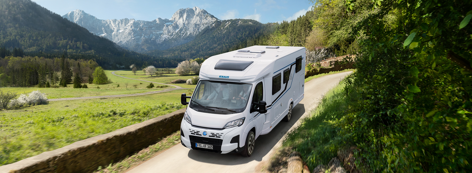A KNAUS SKY TI drives along a road through the green countryside.