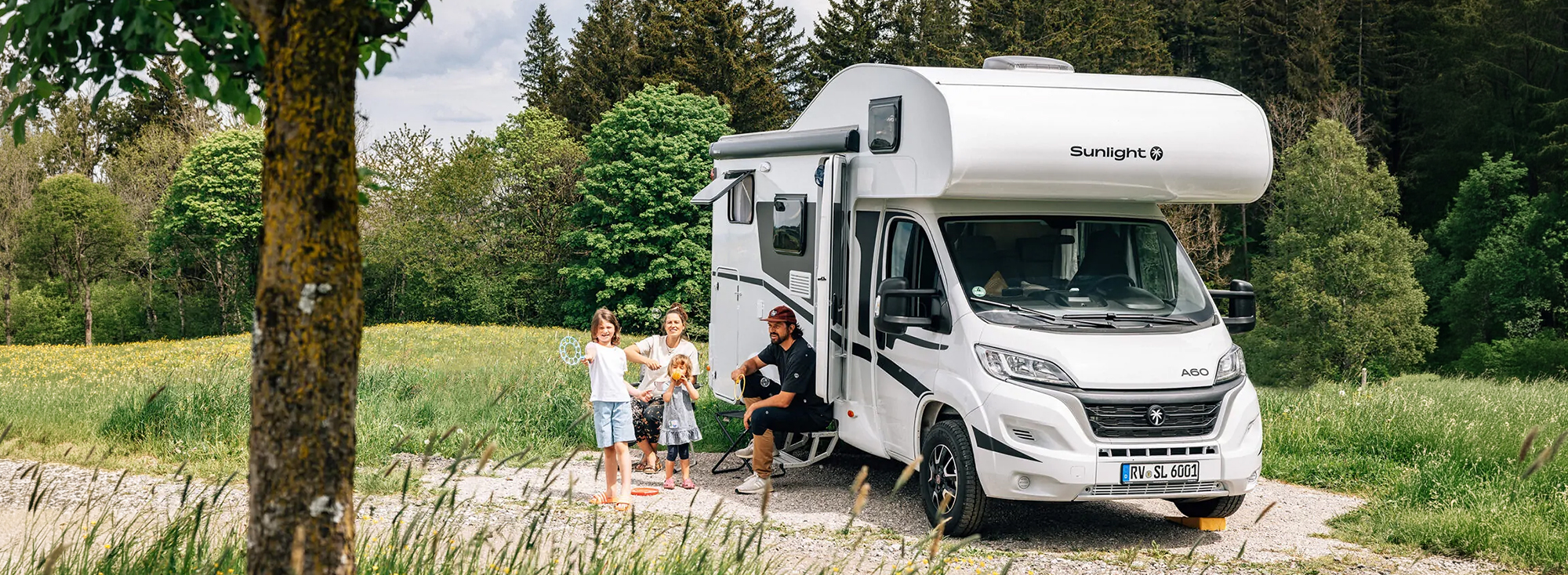 Alkoven-Wohnmobil steht in der Natur und eine Familie befindet sich davor.