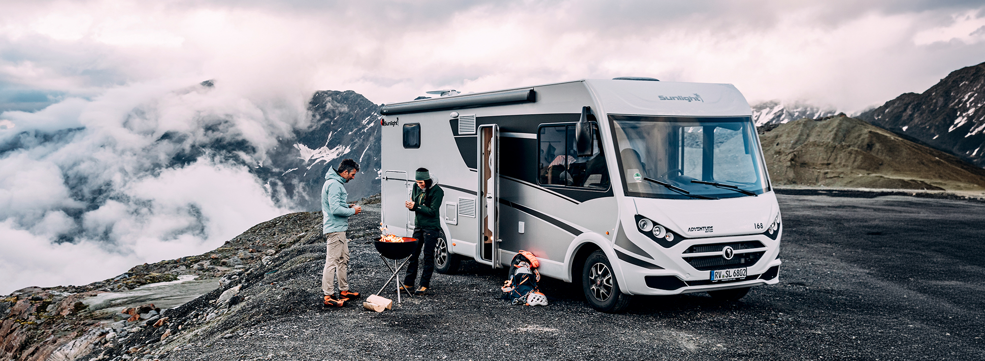 Integriertes Wohnmobil steht in einer Berglandschaft und zwei Personen stehen davor.