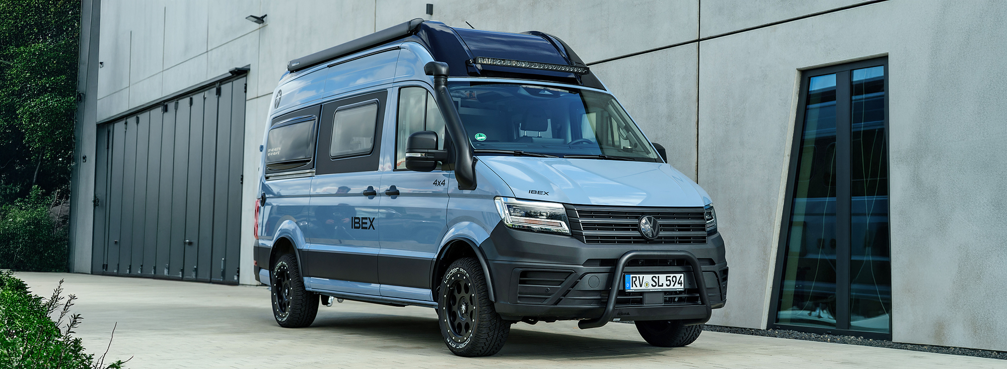 Blauer Camper Van vor einem Industriegebäude.