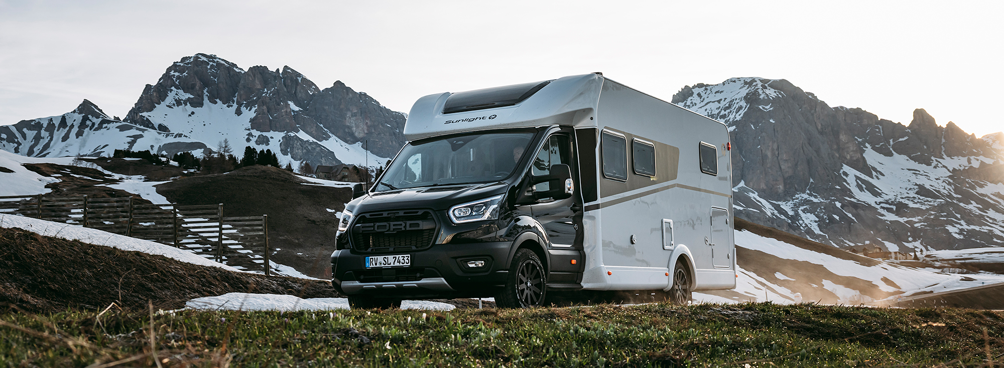Wohnmobil mit dunklem Chassis und weißem Aufbau in einer Bergkulisse.