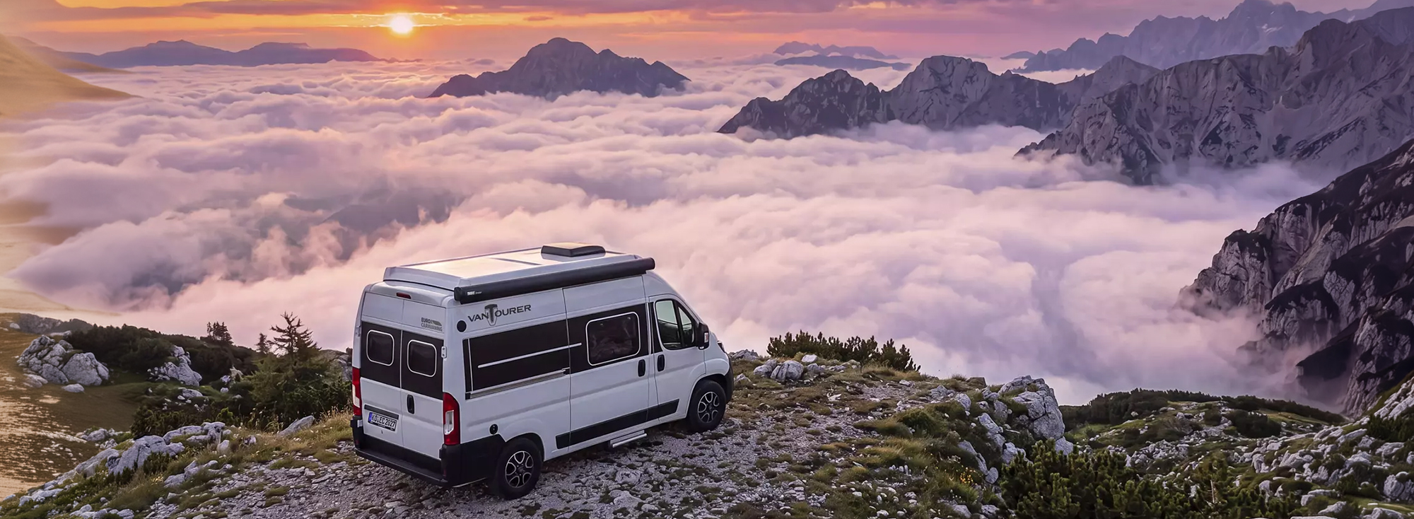 Ein heller Camper Van in einer Berglandschaft über den Wolken.