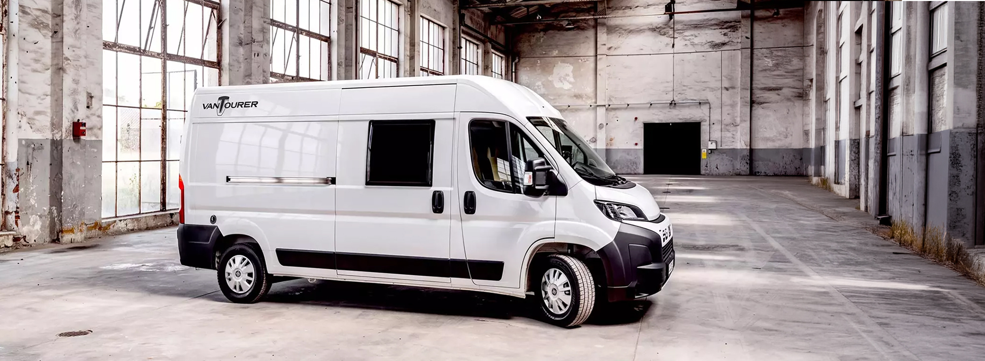 Ein weißer Camper Van in einer Industriehalle. 