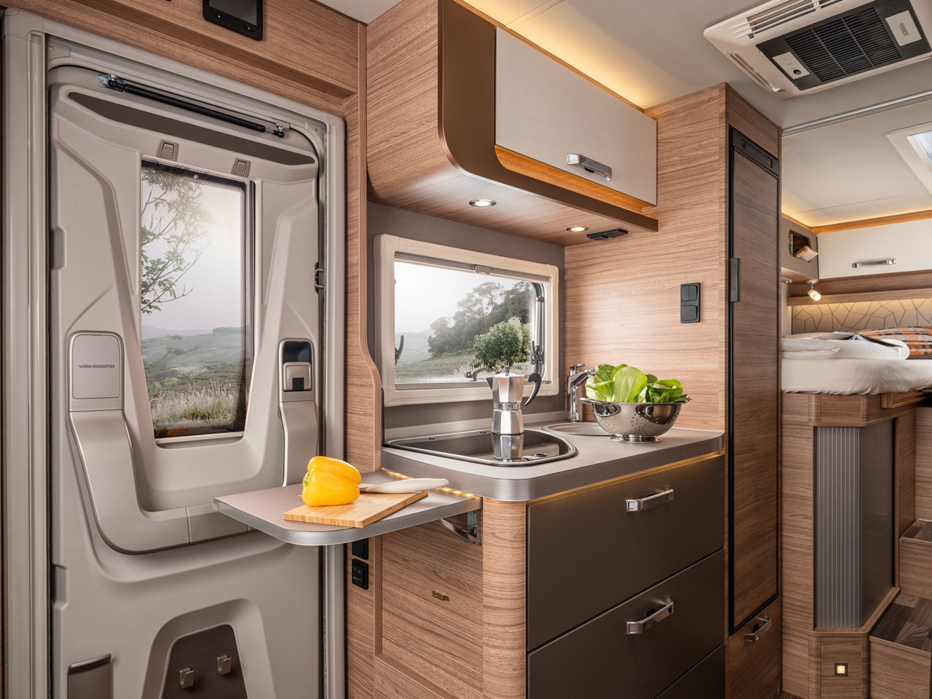 Die Küche eines Wohnmobils in der eine gelbe Paprika und Salat in einem Sieb stehen