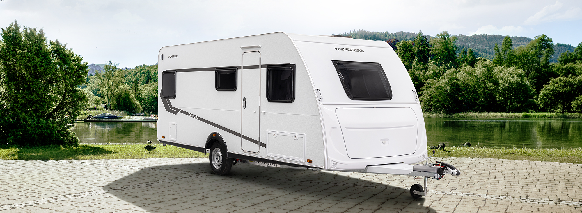 Een witte caravan staat op een erf.