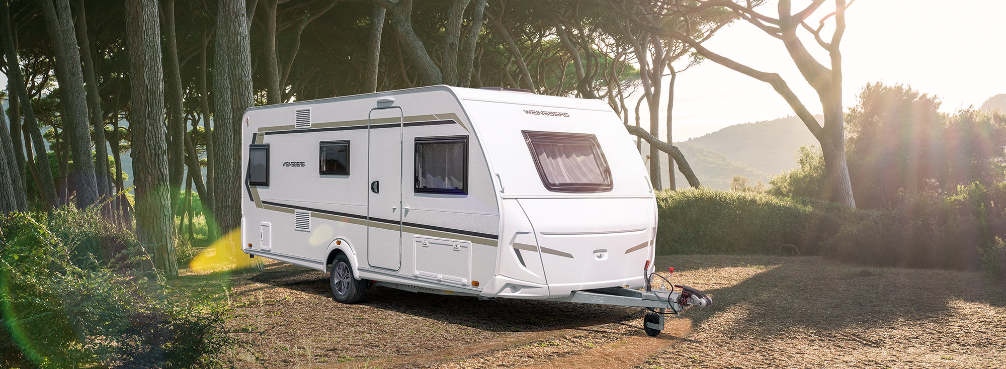 Een witte caravan staat voor een mediterraan bos.