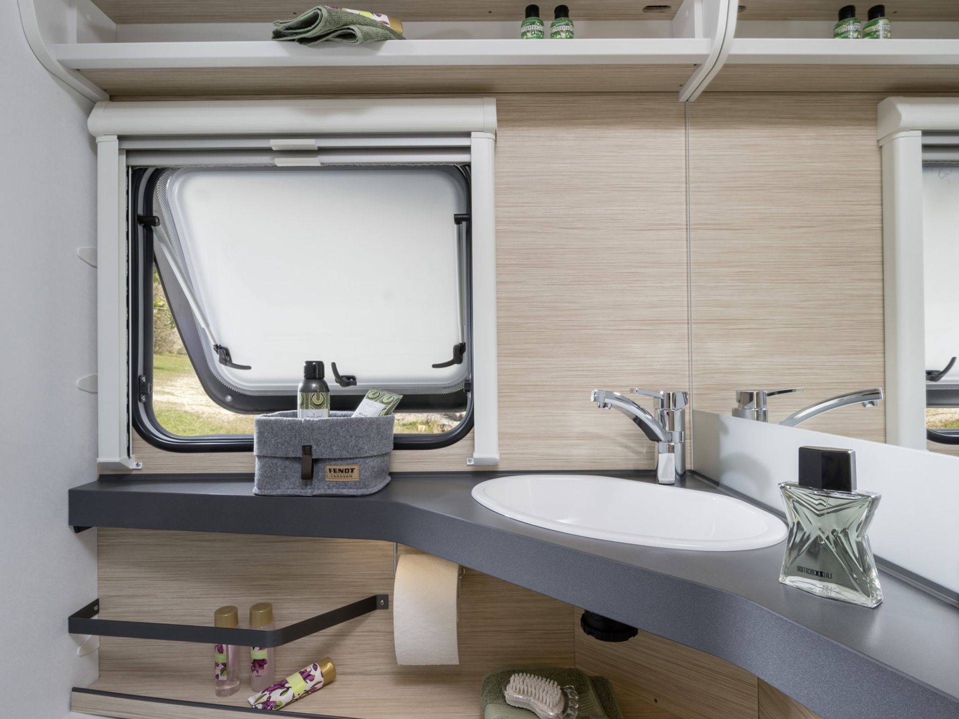 Badezimmer im Wohnwagen mit geoeffnetem Fenster und Baduntensilien neben dem Waschbecken.